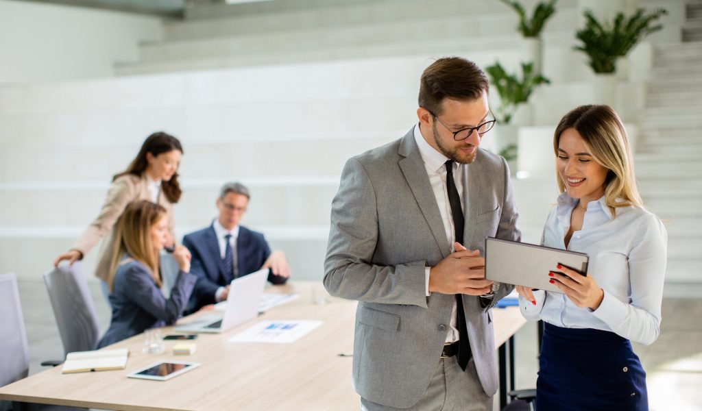 Handsome young business couple looking at financial results on digital tablet in front of their team at the office